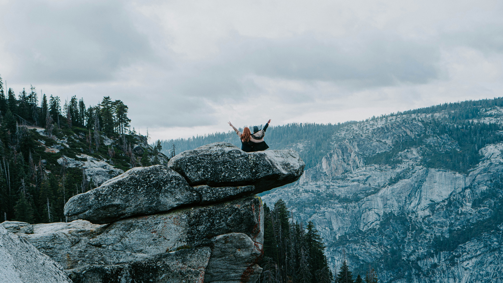 An image showing two people sitting on a ledge in the wilderness.